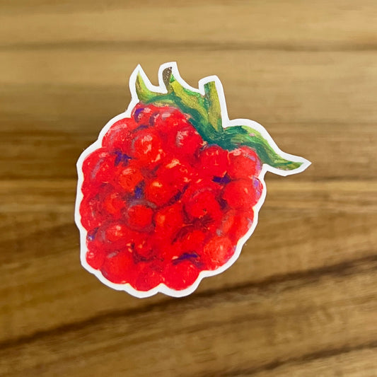 Sticker of a red raspberry with green leaves on a wooden surface