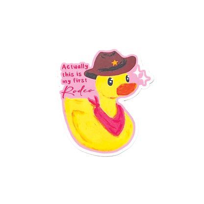 Yellow rubber duck wearing a cowboy hat and bandana with text 'actually this is my first rodeo' on a white background
