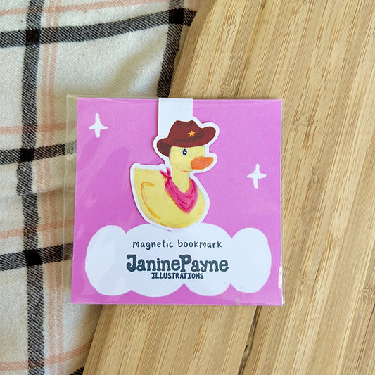Pink packaging of a magnetic bookmark with a duck illustration on a wooden surface.