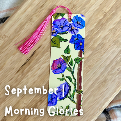 Bookmark with blue flowers and pink tassel on a wooden surface, labeled 'September Morning Glories'.
