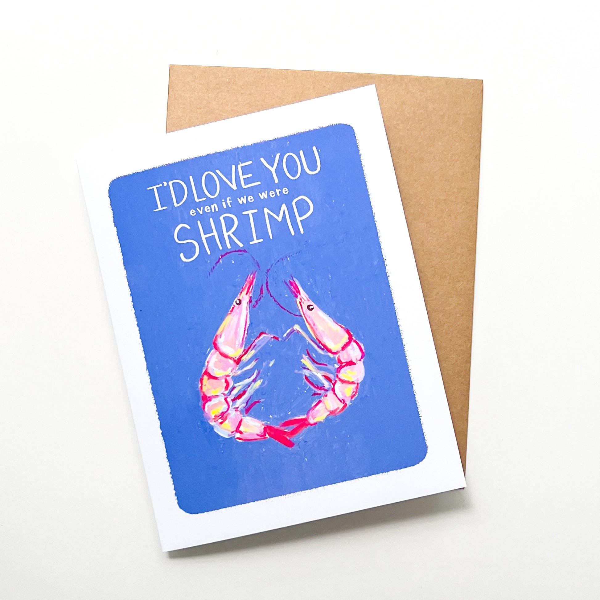 Greeting card with shrimp illustration and text 'I'd love you even if we were shrimp' on a blue background, with a brown envelope.
