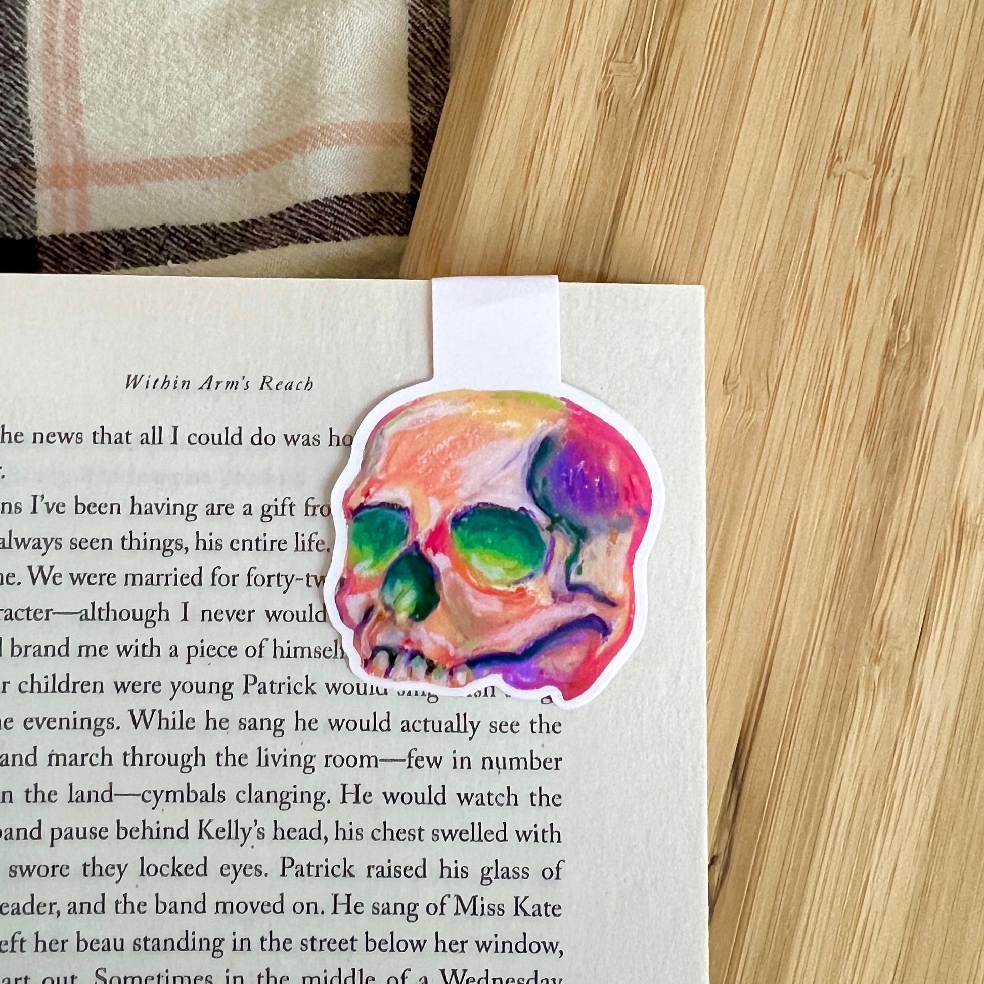 Colorful skull magnetic bookmark on a book page with a wooden surface and plaid fabric in the background