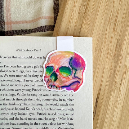 Colorful skull magnetic bookmark on a book page with a wooden surface and plaid fabric in the background