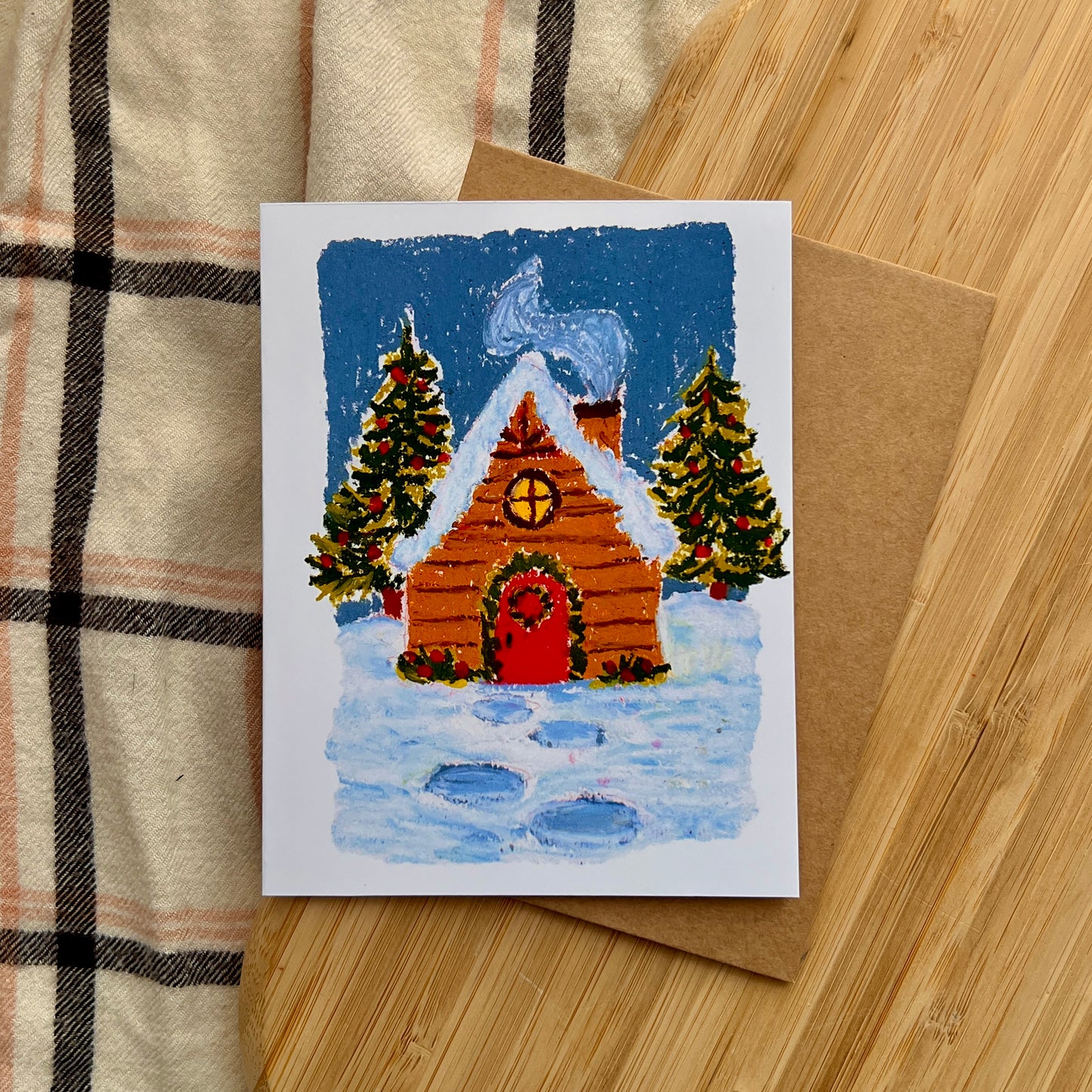 Christmas card with a wooden cabin and trees on a wooden surface