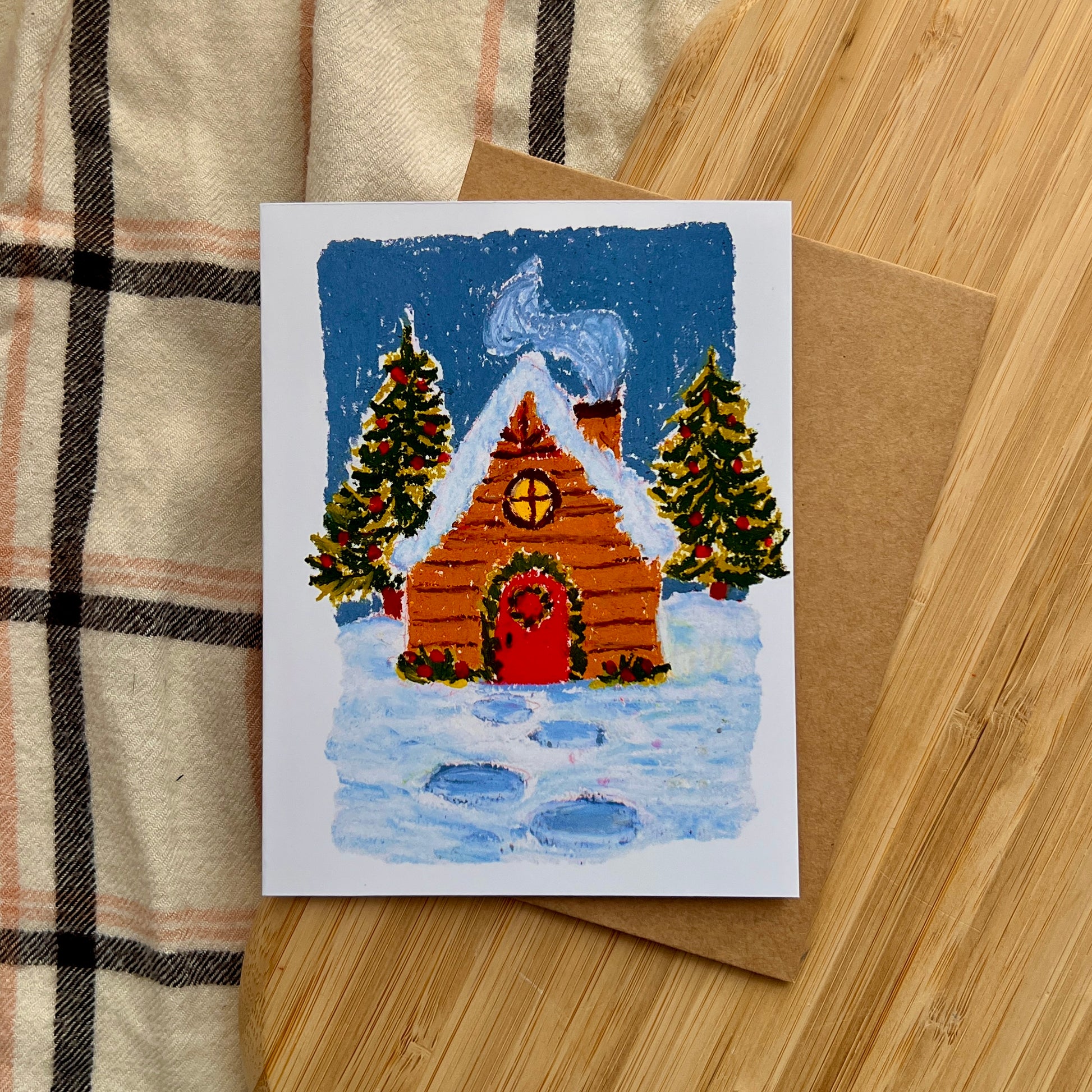 Christmas card with a wooden cabin and trees on a wooden surface