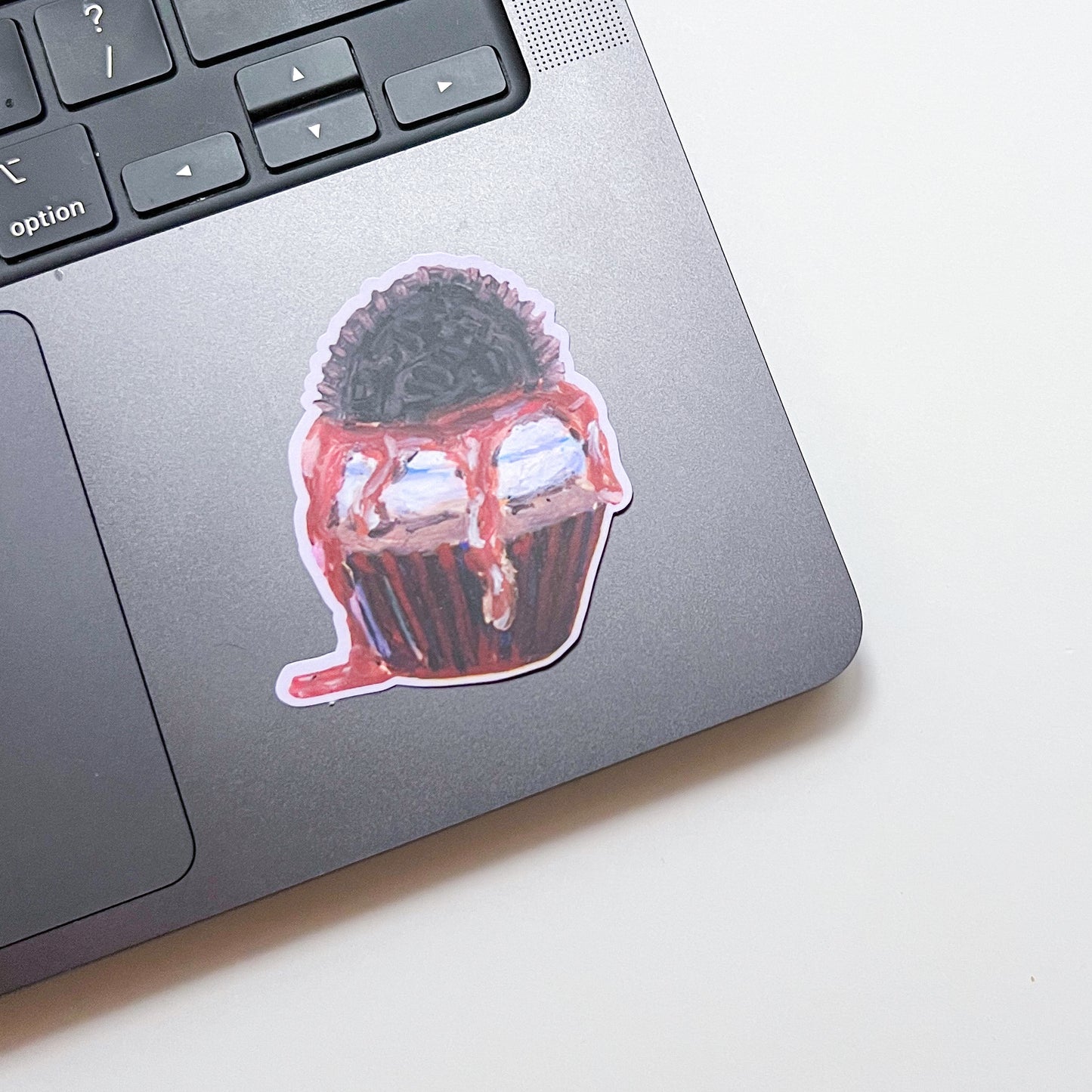 Laptop with a sticker of a cupcake and black hair on a white surface