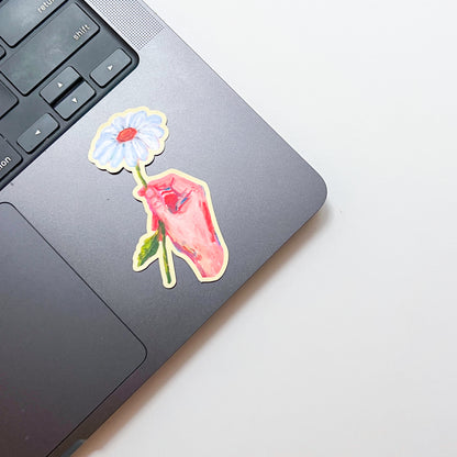Laptop with a colorful sticker of a hand holding a flower on a light gray background
