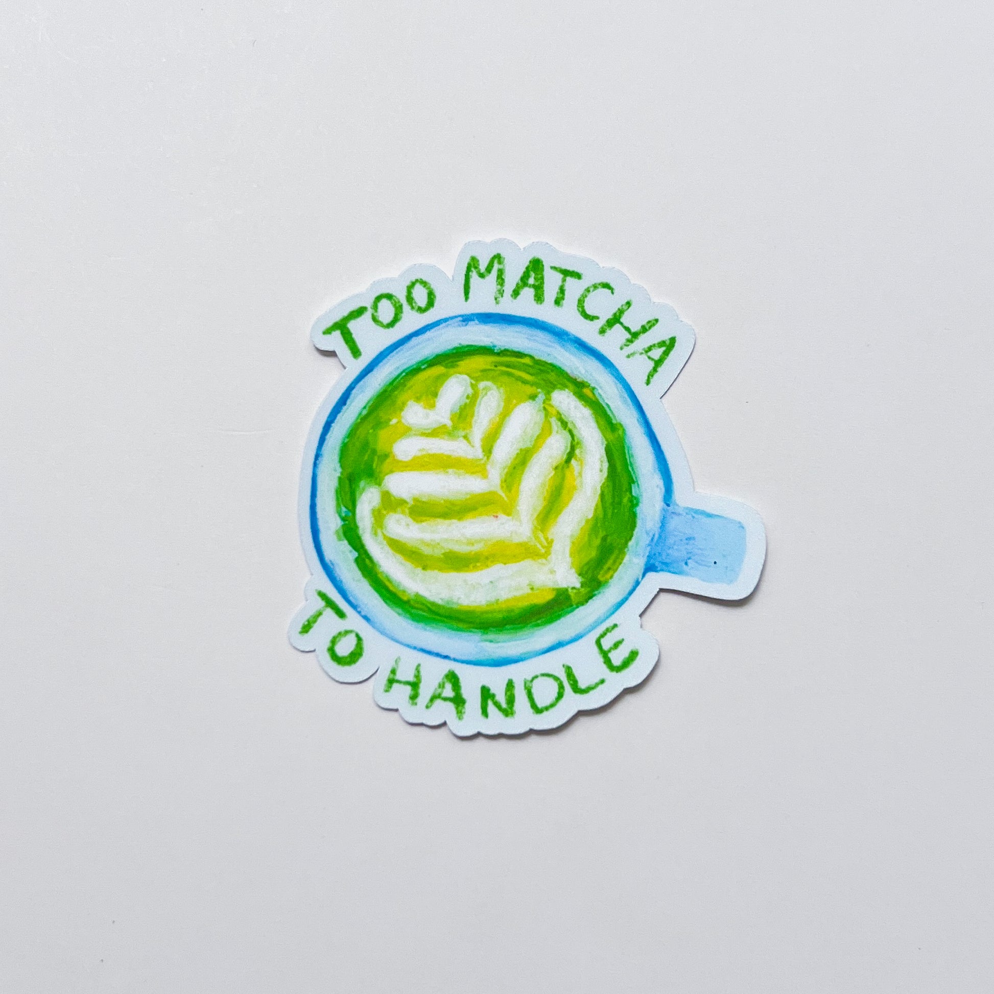 Sticker with a matcha latte design and text 'Too Matcha To Handle' on a light gray background