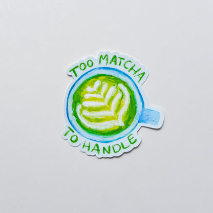 Sticker with a matcha latte design and text 'Too Matcha To Handle' on a light gray background
