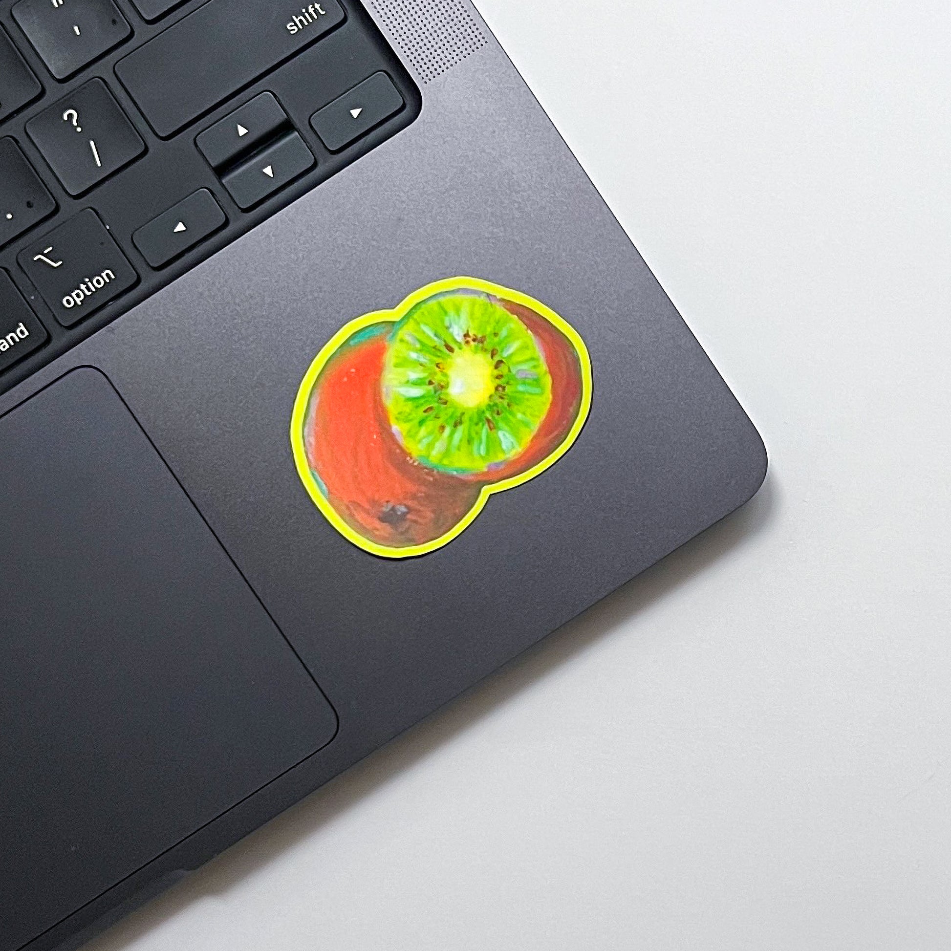 Laptop with a colorful sticker of a kiwi fruit on a light gray background