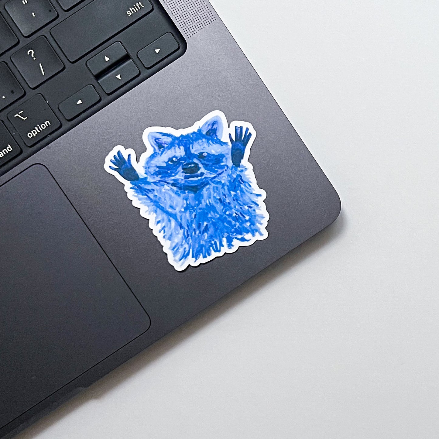Blue raccoon sticker on a laptop trackpad