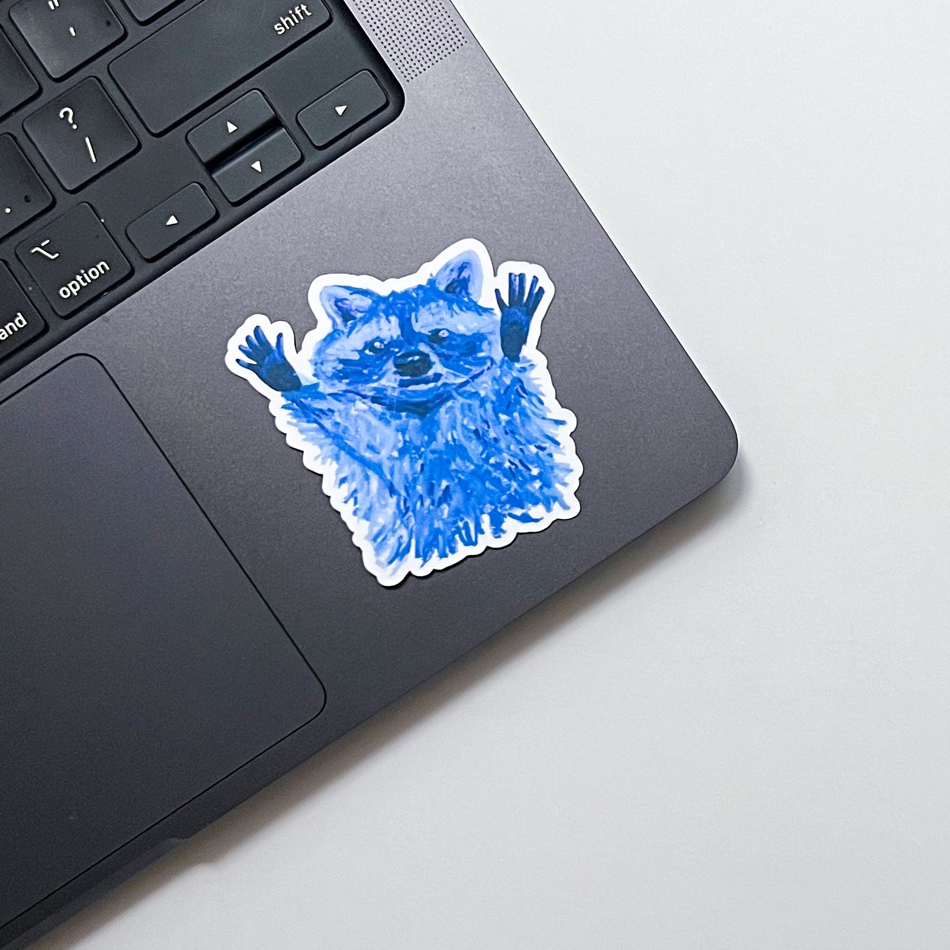 Blue raccoon sticker on a laptop trackpad