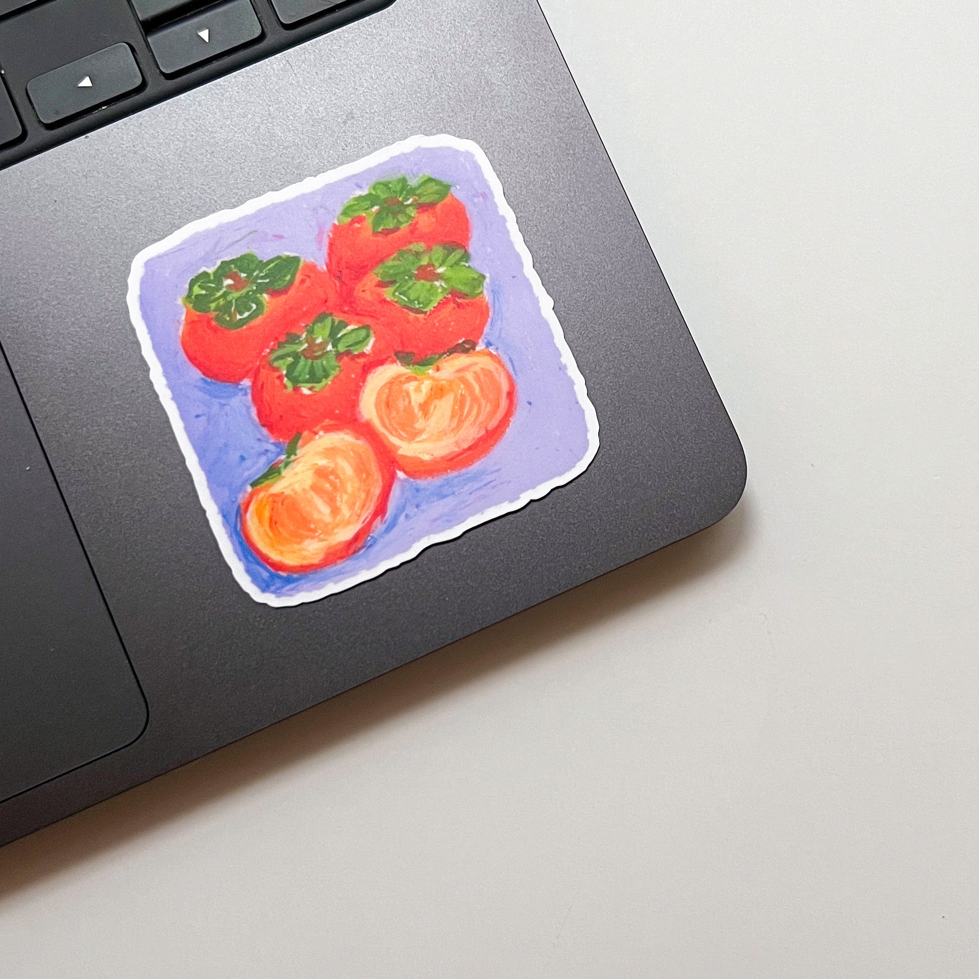 Laptop trackpad with a sticker of persimmons on a light gray surface