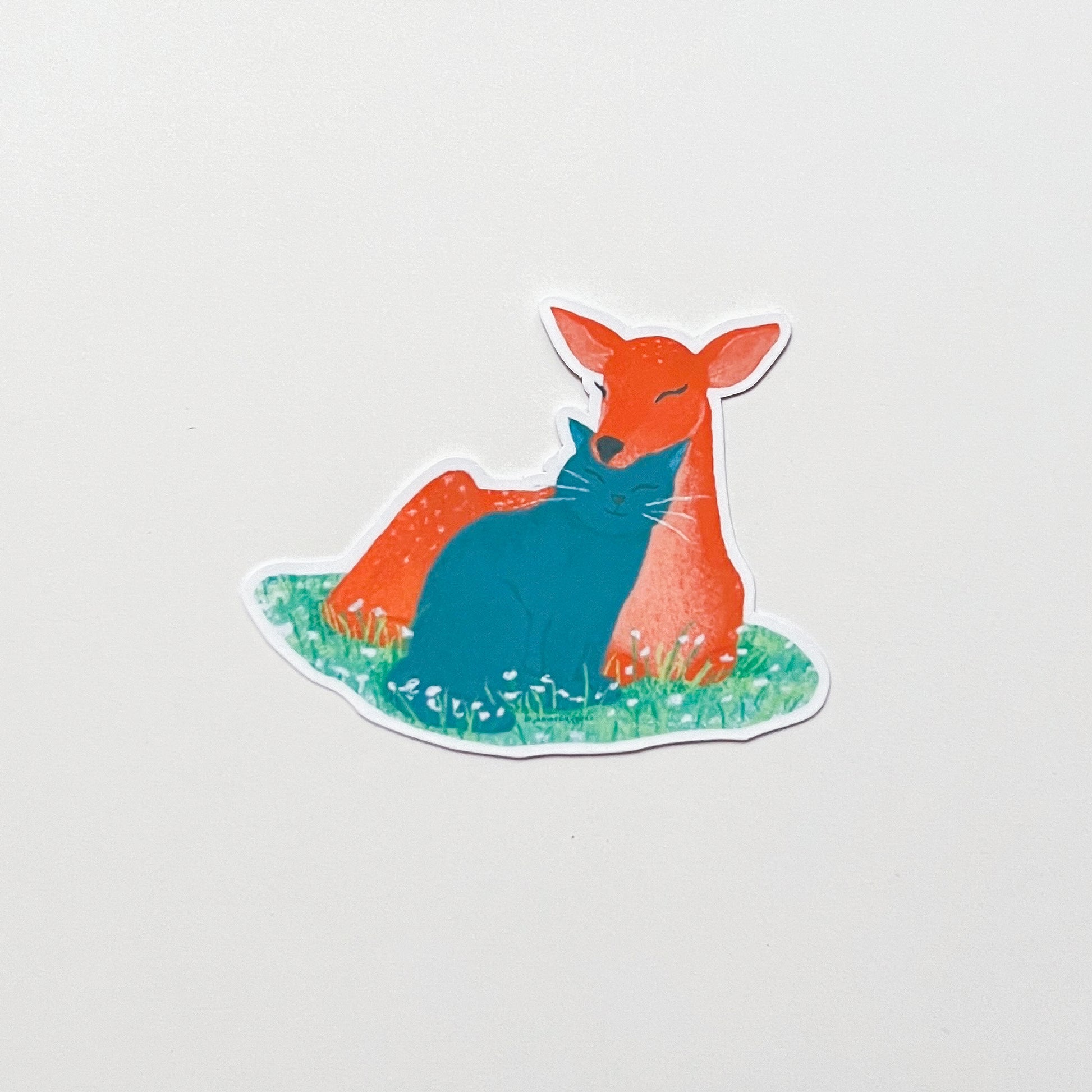 Sticker of a deer and cat sitting on grass with a light grey background