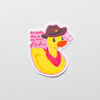 Sticker of a rubber duck wearing a cowboy hat and bandana with text on a light gray background