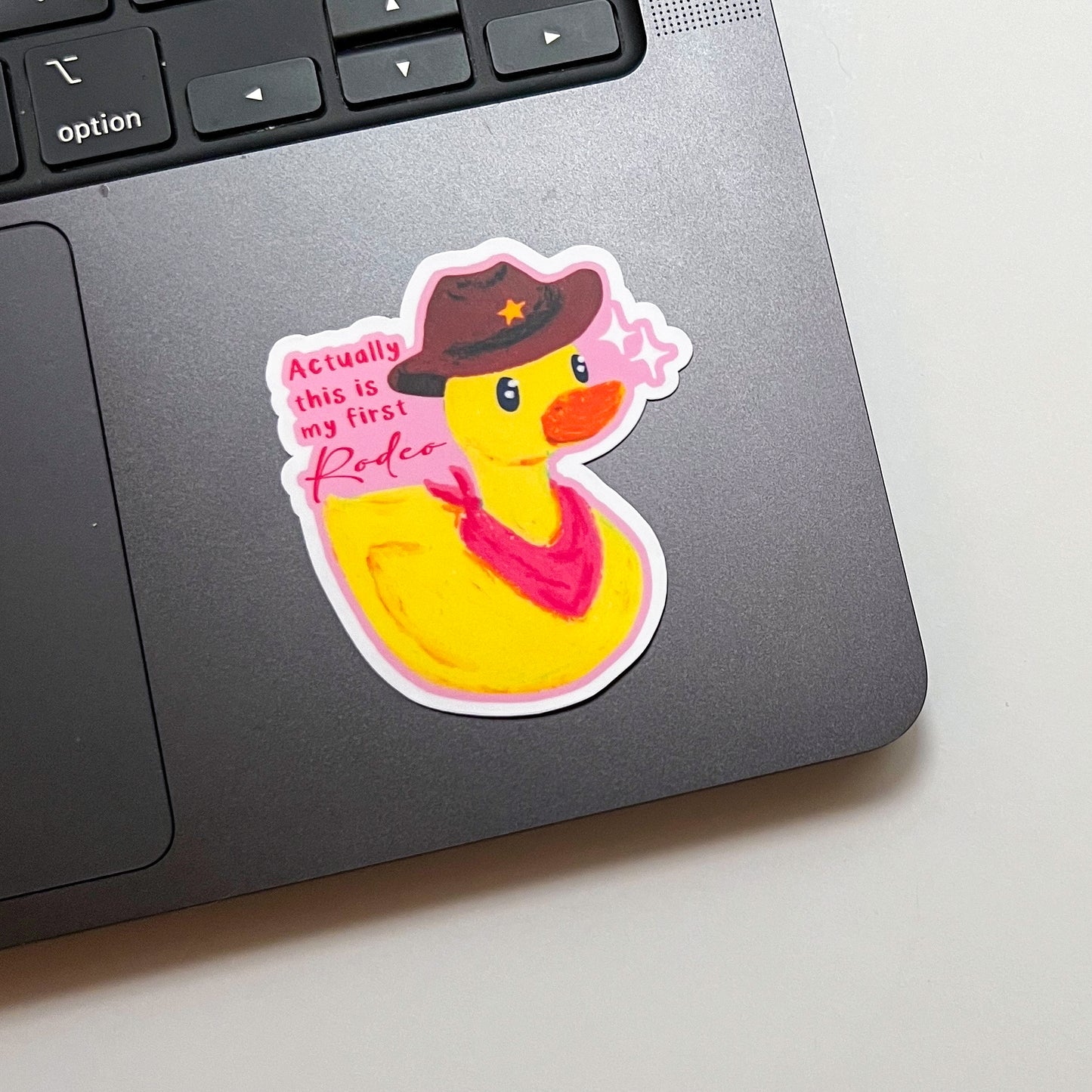 Sticker of a yellow rubber duck wearing a cowboy hat and bandana on a laptop.