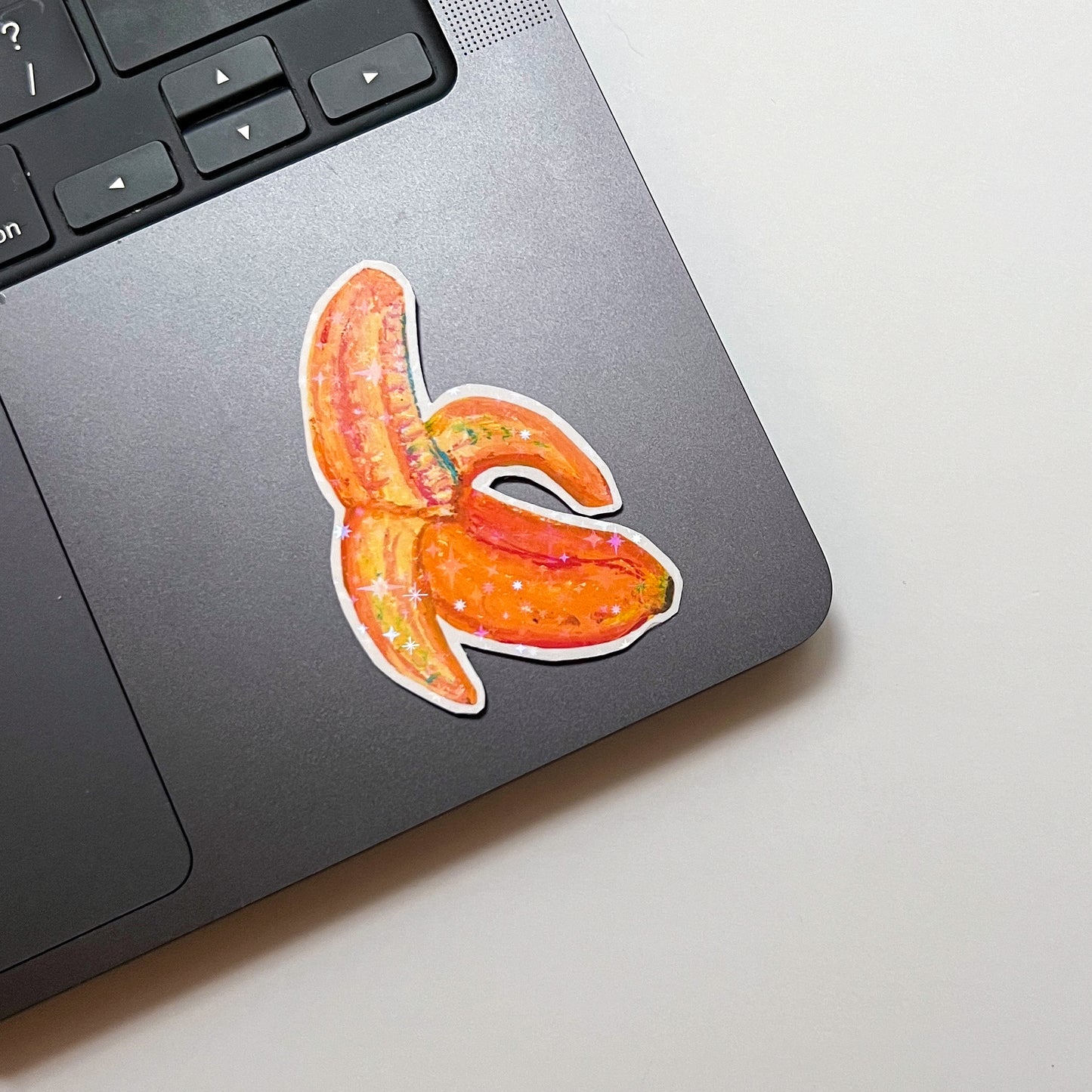 Laptop with a colourful banana sticker on a light surface