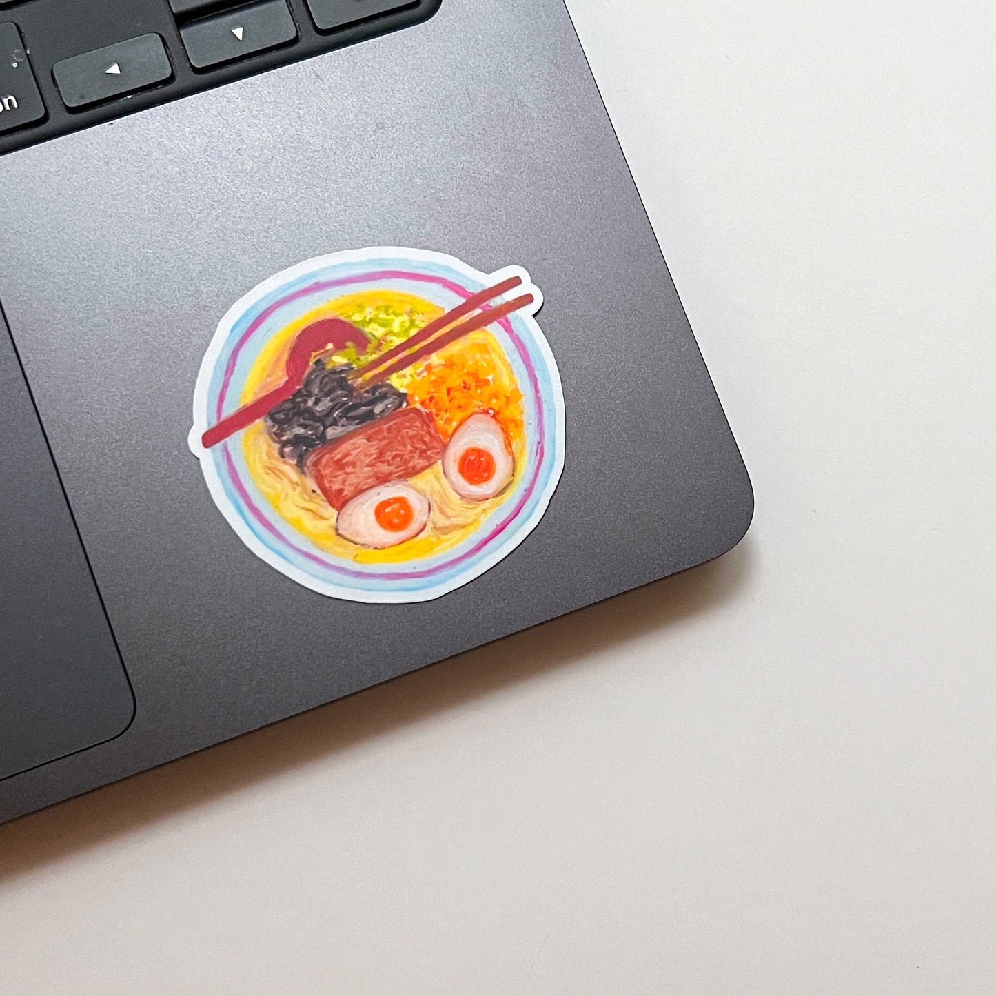Laptop with a sticker of a bowl of ramen on a light surface
