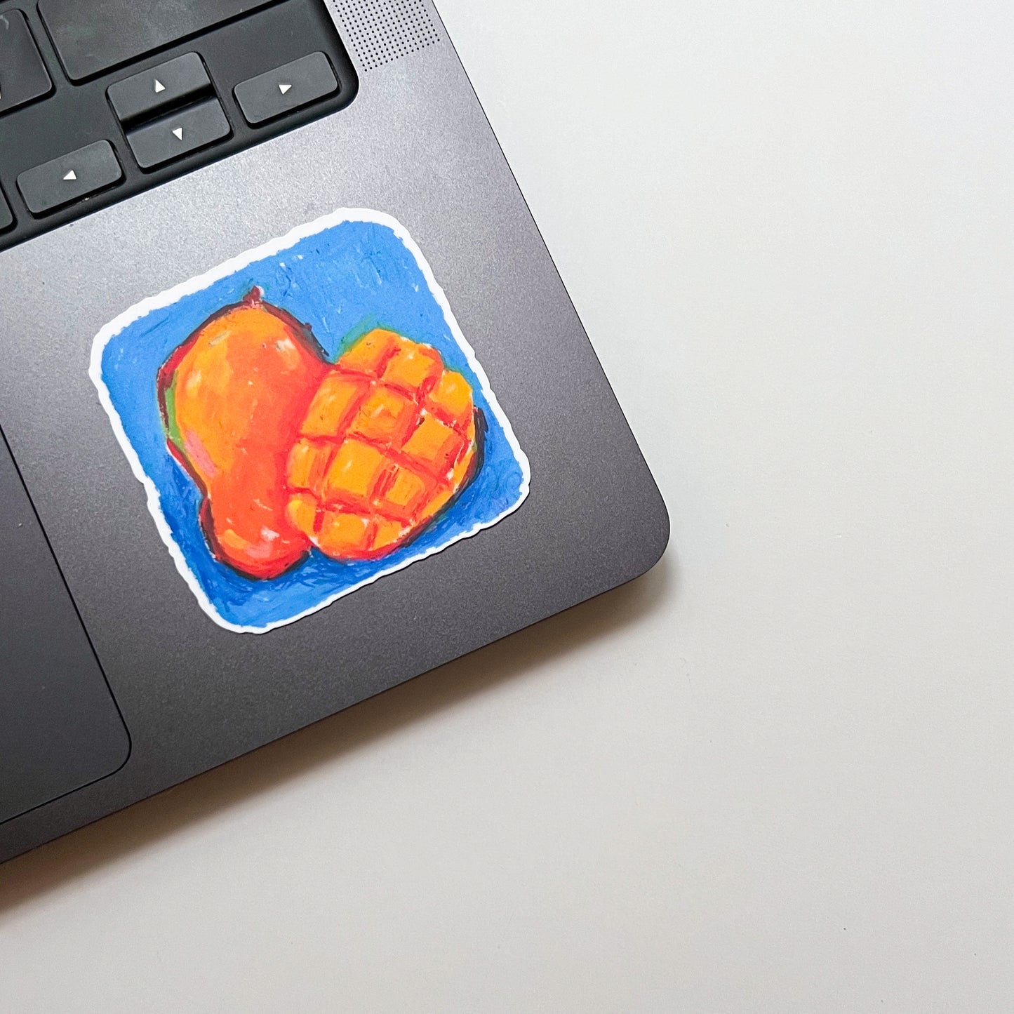 Laptop with a colorful sticker of a mango on a light surface