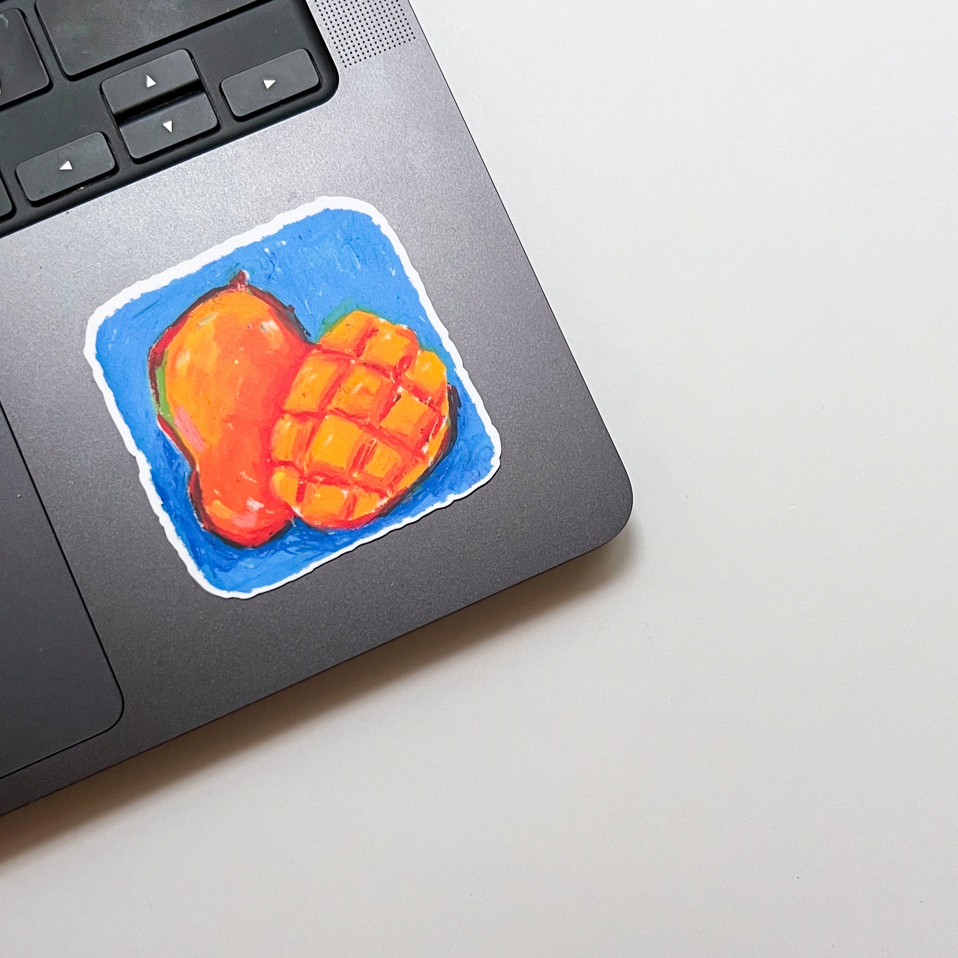 Laptop with a colorful sticker of a mango on a light surface