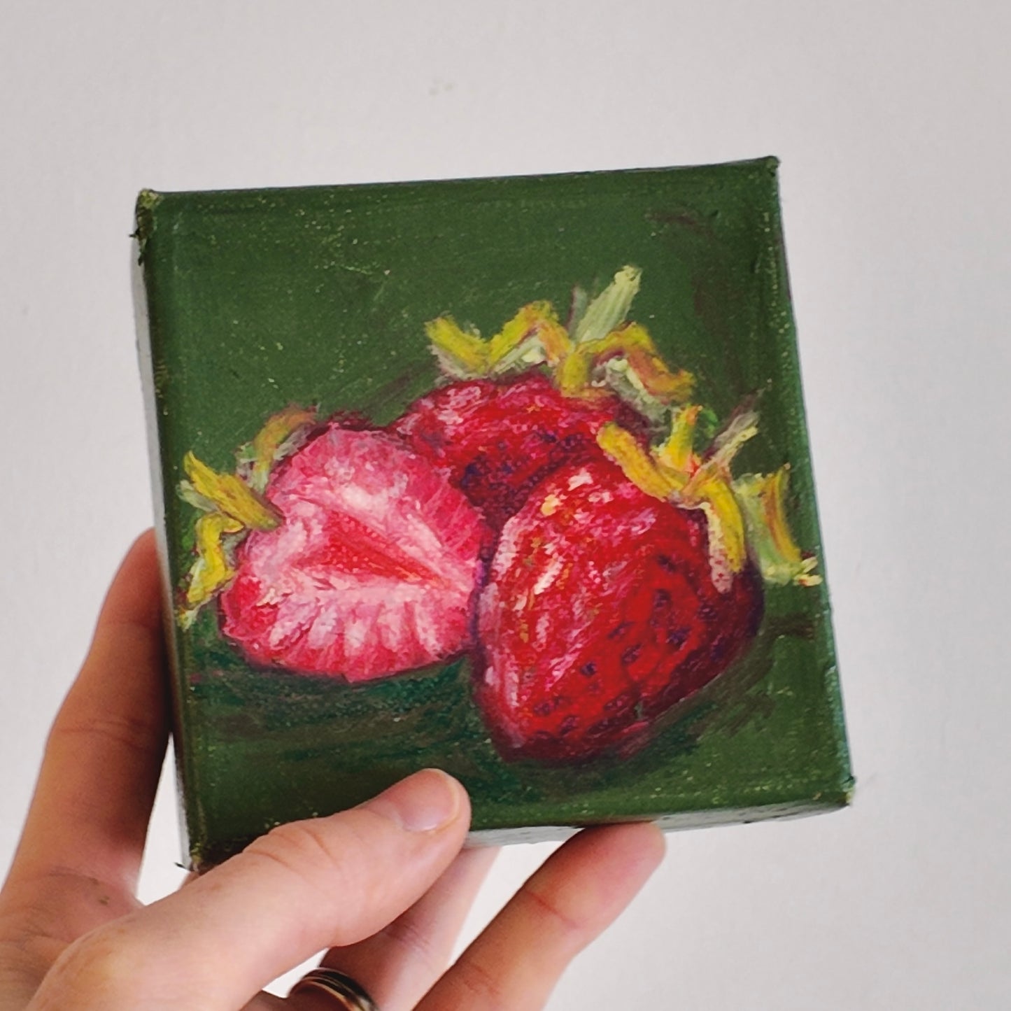Small painting of strawberries held by a hand on a light gray background