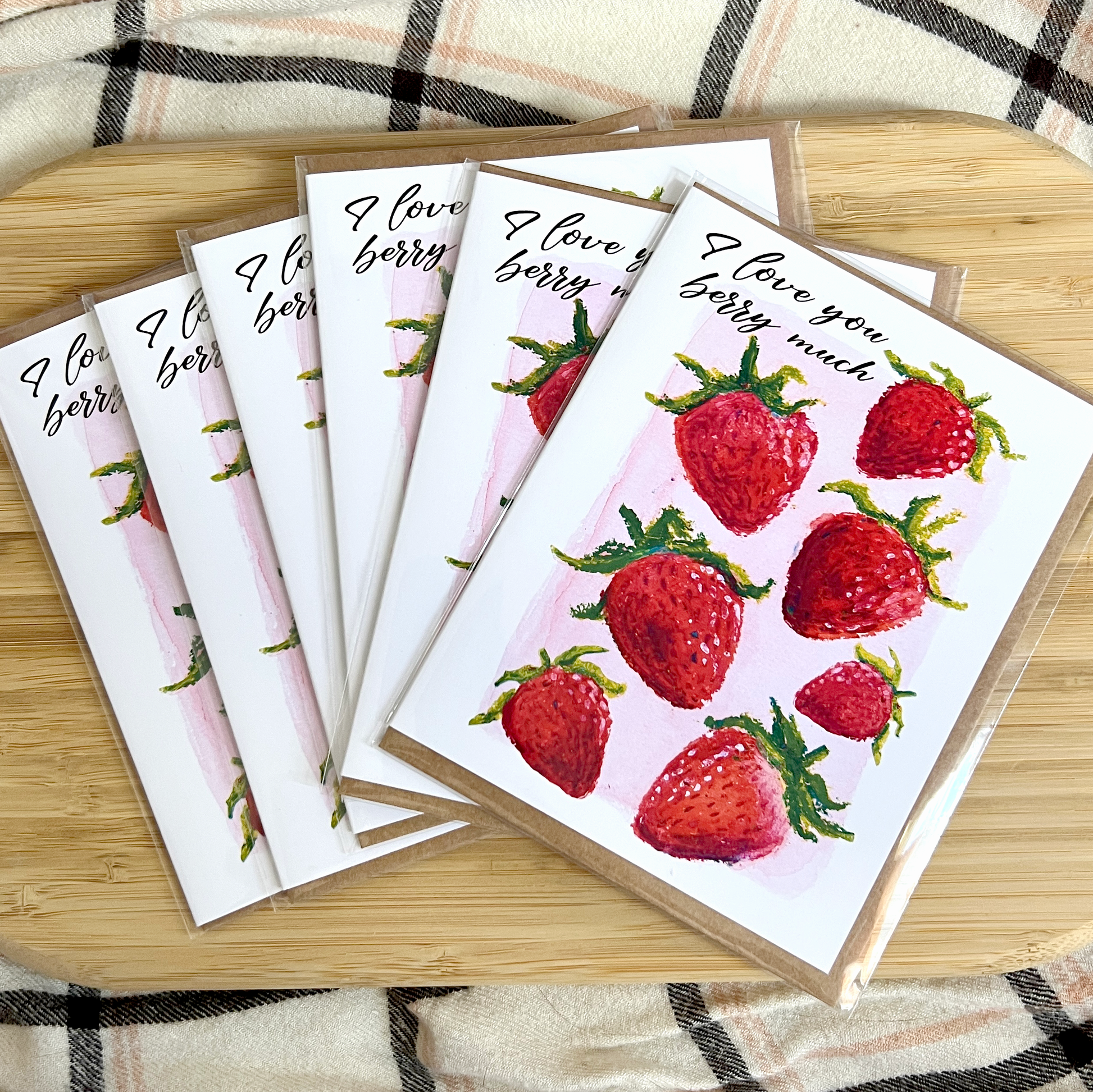 Set of greeting cards with strawberry design and 'I love you berry much' text on a wooden surface.
