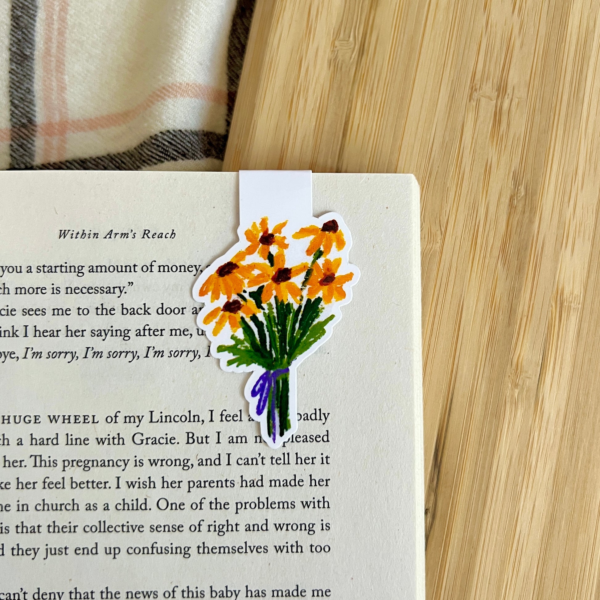 Floral bookmark on a book with a wooden surface and plaid fabric in the background