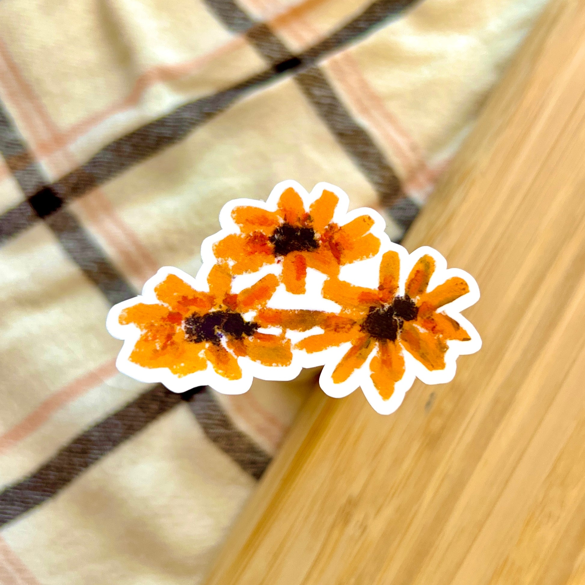 Three orange flower shaped stickers on a checkered fabric background