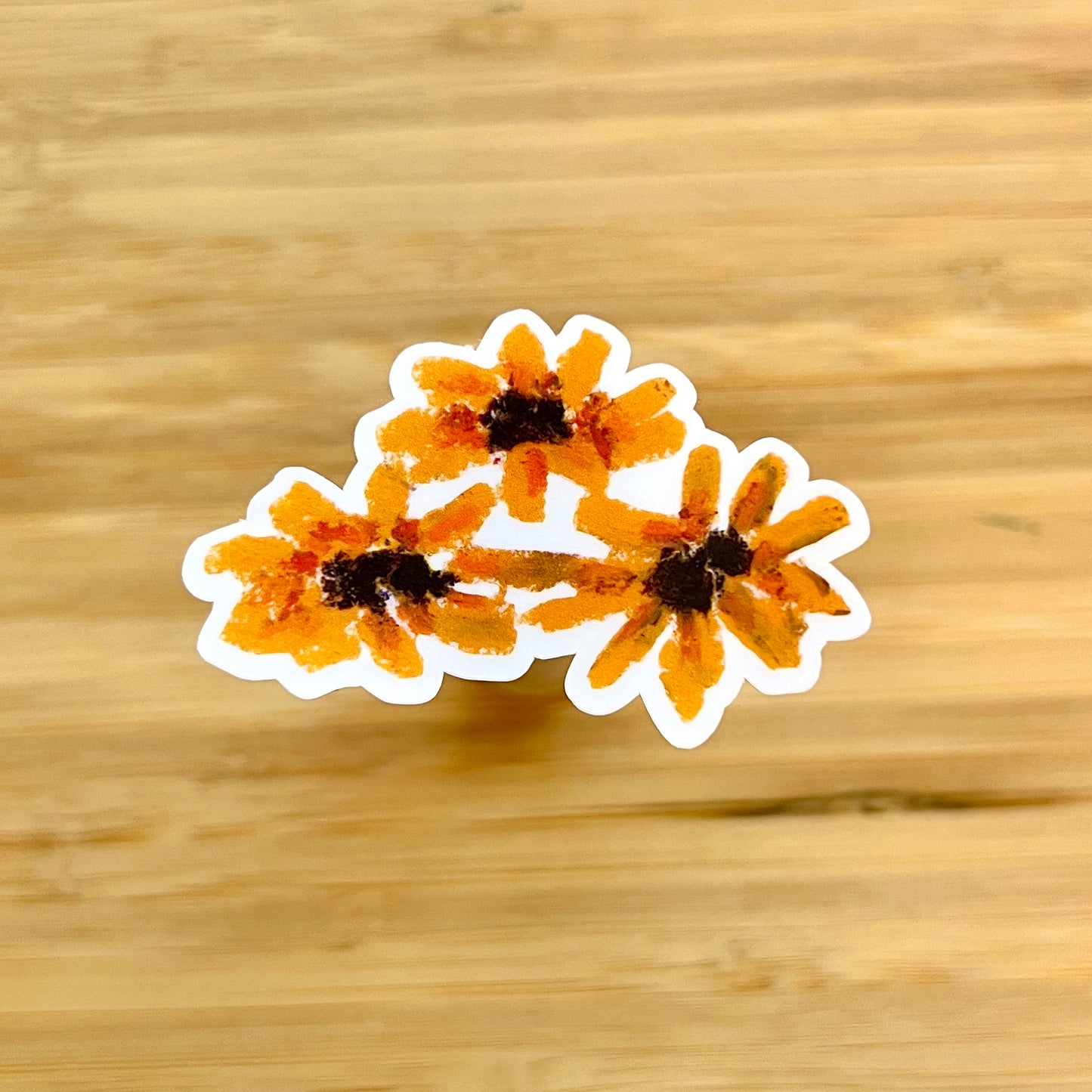 Three orange flowers with black centers on a wooden surface