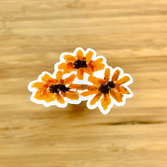 Three orange flowers with black centers on a wooden surface