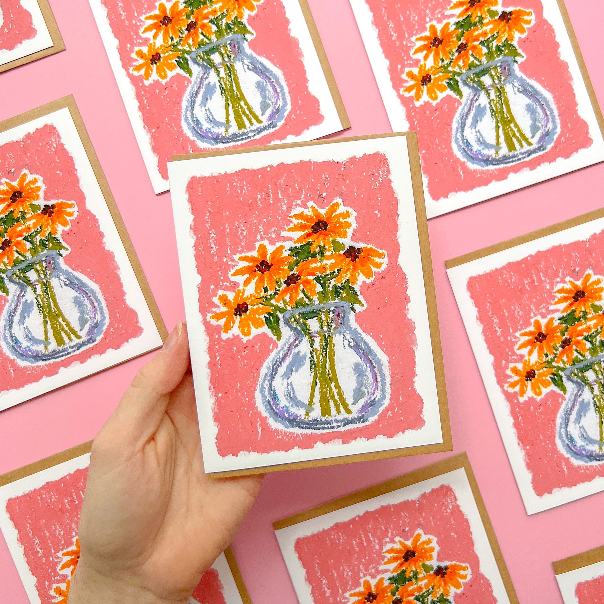 hand holding a greeting card with an oil pastel drawing of a flower vase