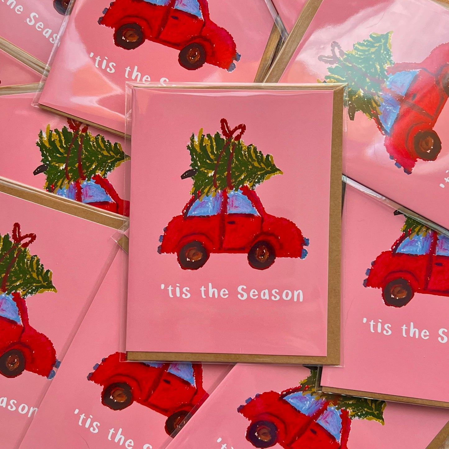 Stack of Christmas cards with red cars and trees on pink backgrounds.