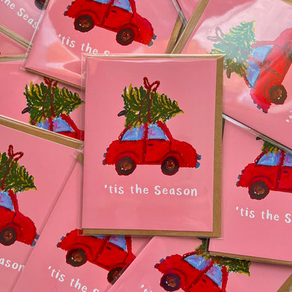 Stack of Christmas cards with red cars and trees on pink backgrounds.