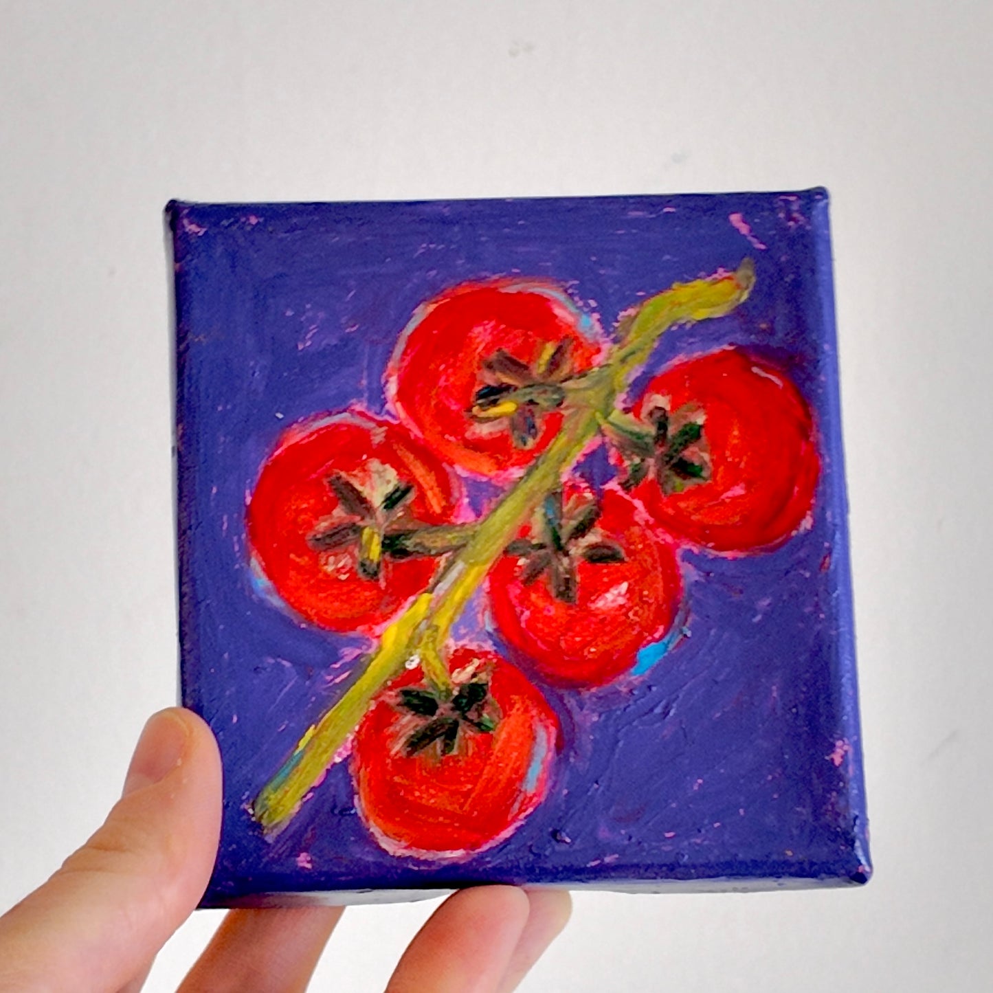 Small painting of red tomatoes on a purple background held by a hand.