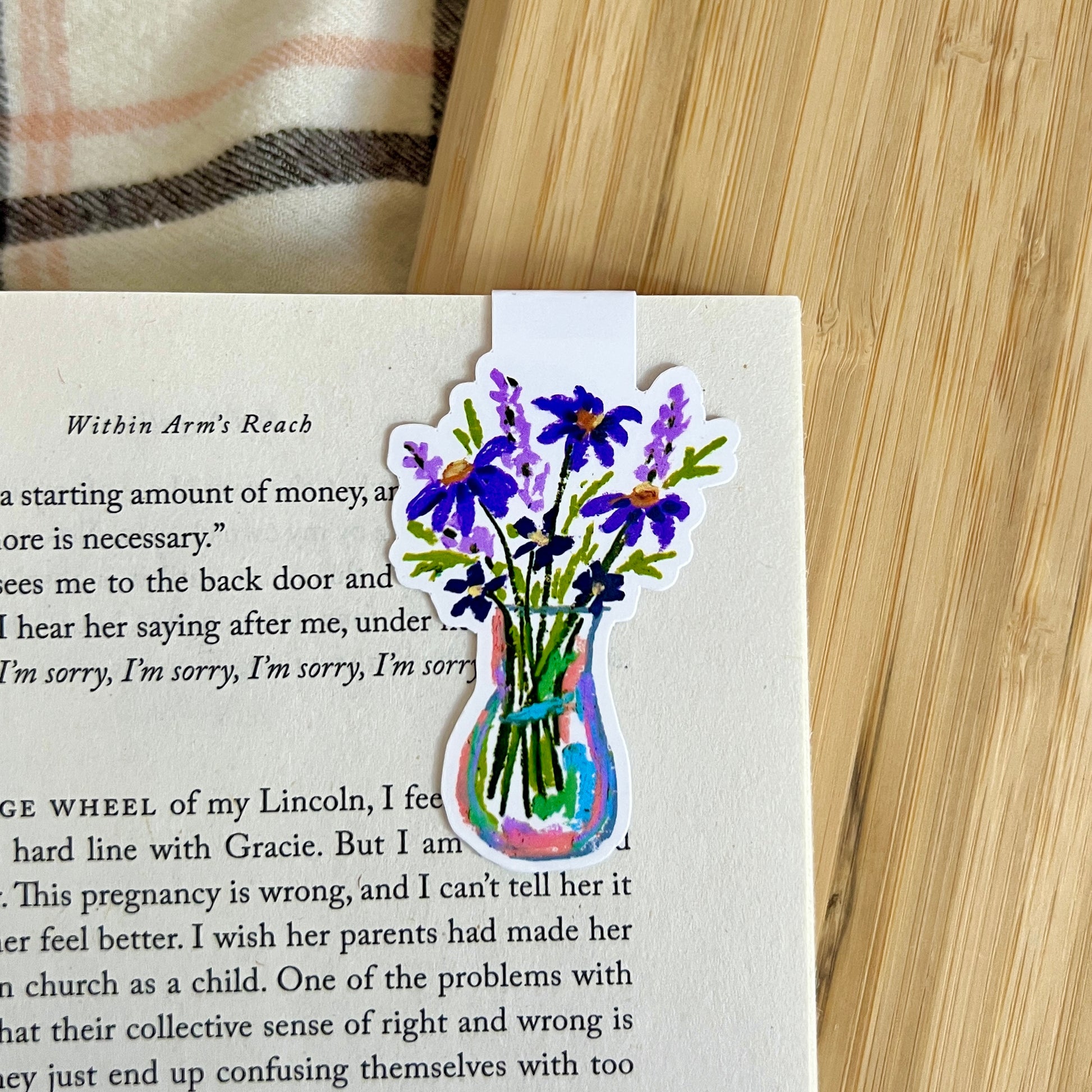 Floral sticker on a book page with a wooden surface and plaid fabric in the background