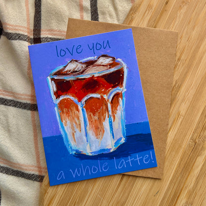 Card with a drawing of a glass of iced coffee and text 'love you a whole latte!' on a wooden surface.