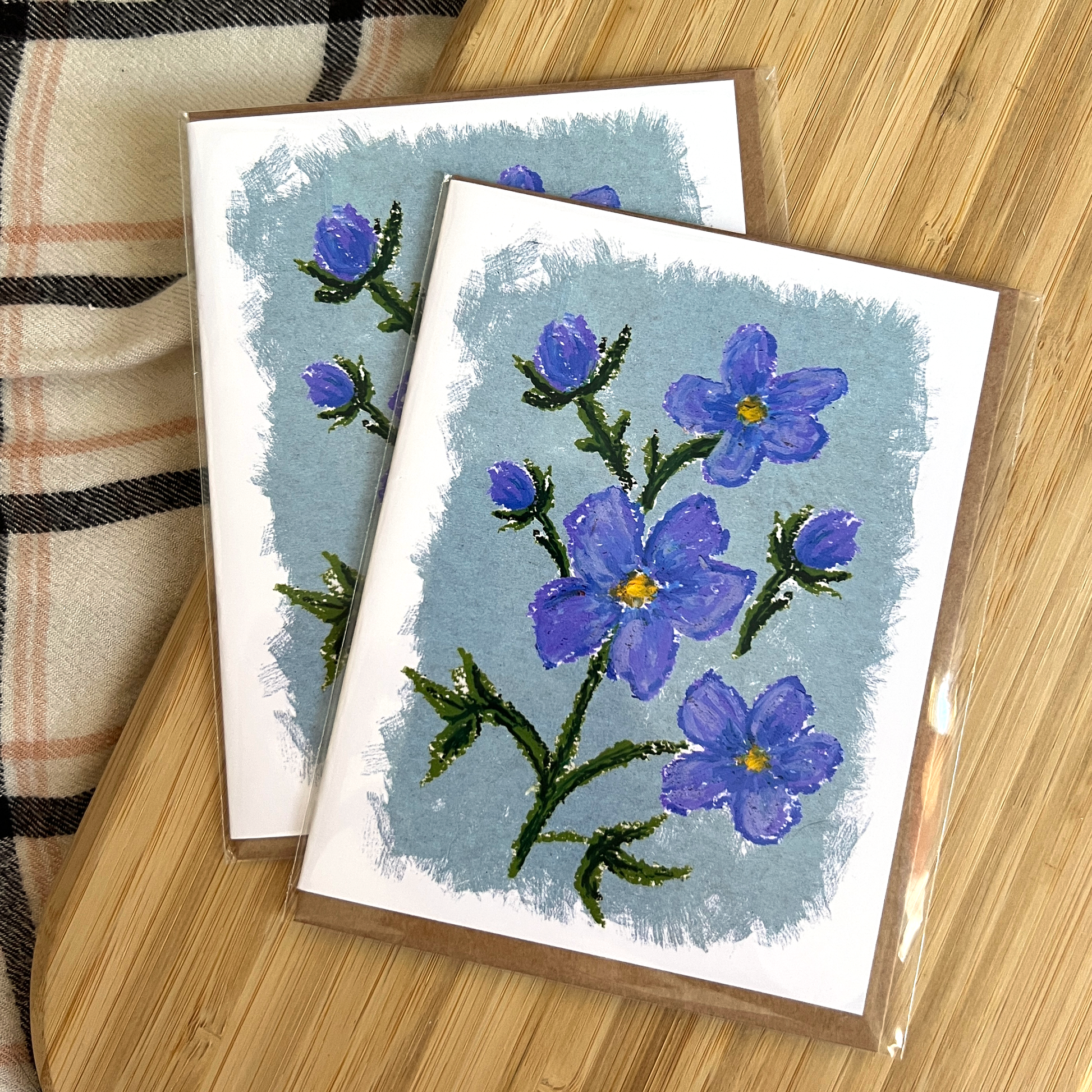 Two greeting cards with blue floral designs on a wooden surface.
