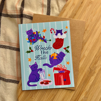 Holiday card with purple cats and festive text 'Wreck the Halls'  on a wooden surface
