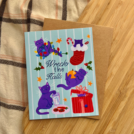 Holiday card with purple cats and festive text 'Wreck the Halls'  on a wooden surface