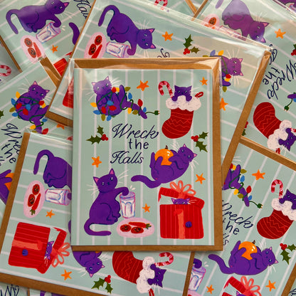 Stack of greeting cards with purple cats and Christmas-themed illustrations on a light blue background.