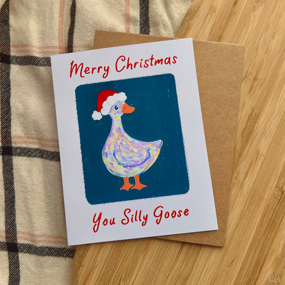 Christmas card with a goose wearing a Santa hat on a wooden surface.