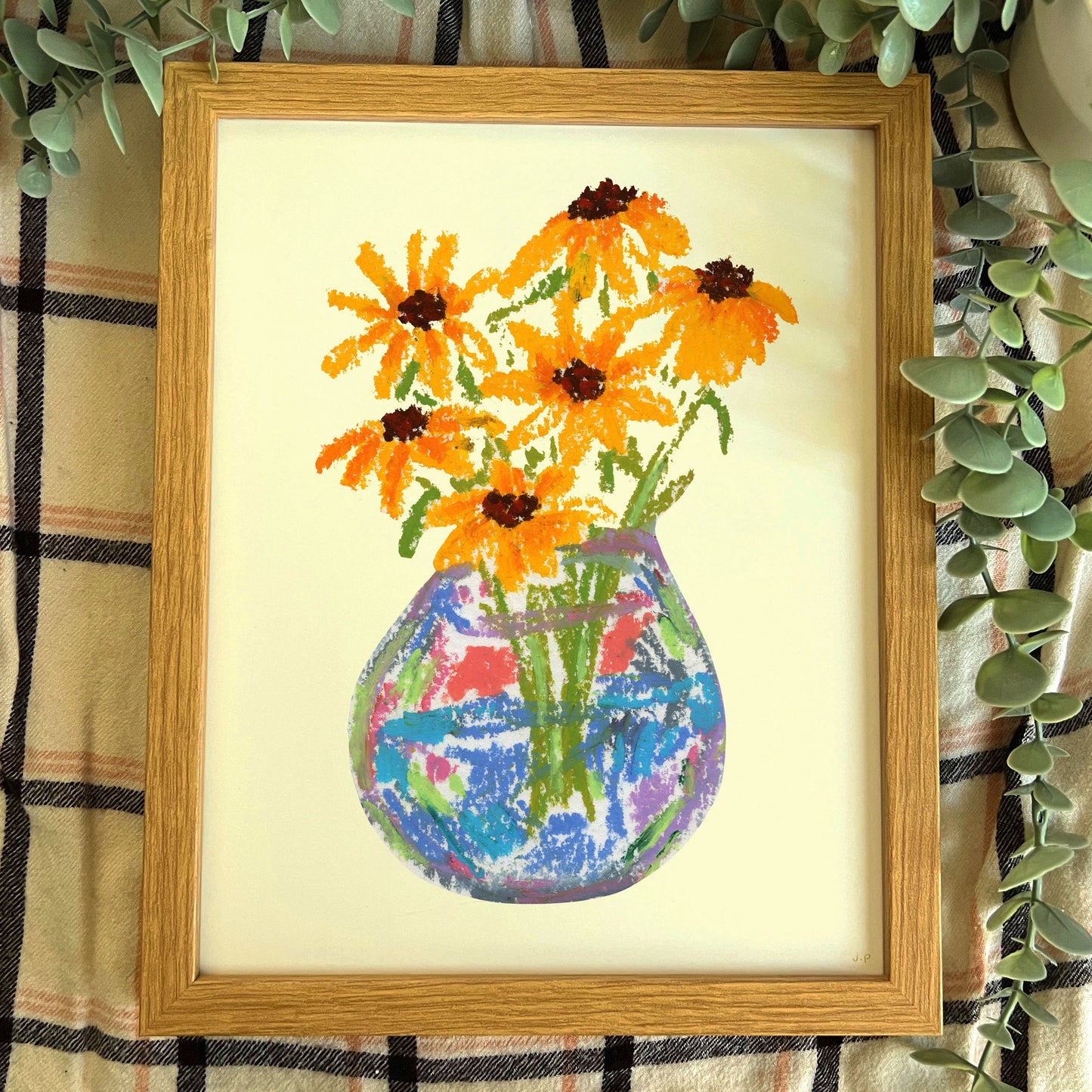 Framed cross-stitched artwork of a vase with flowers on a checkered fabric background