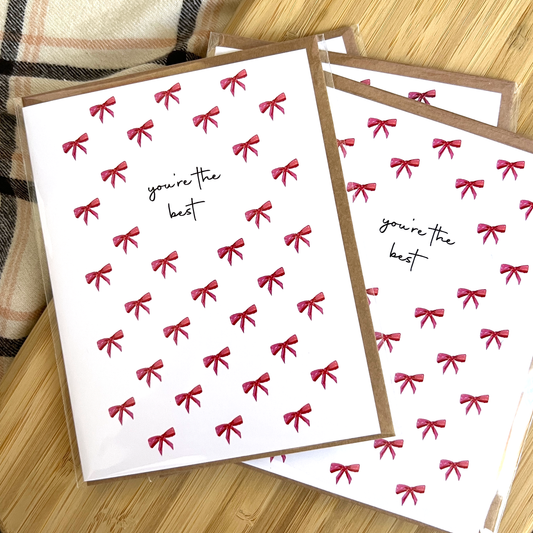 Greeting cards with red bows and 'you're the best' text on a wooden surface.