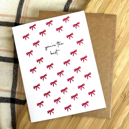 Greeting card with red bows and 'you're the best' text on a wooden surface
